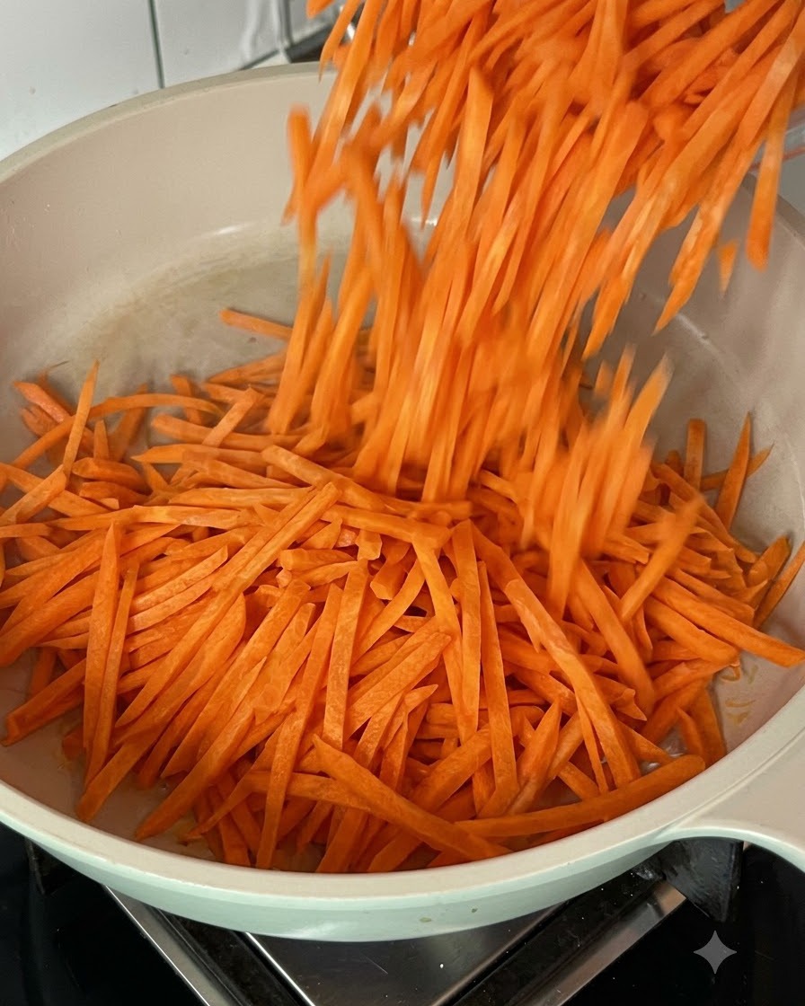 Zanahorias ralladas frescas siendo salteadas en una sartén caliente.