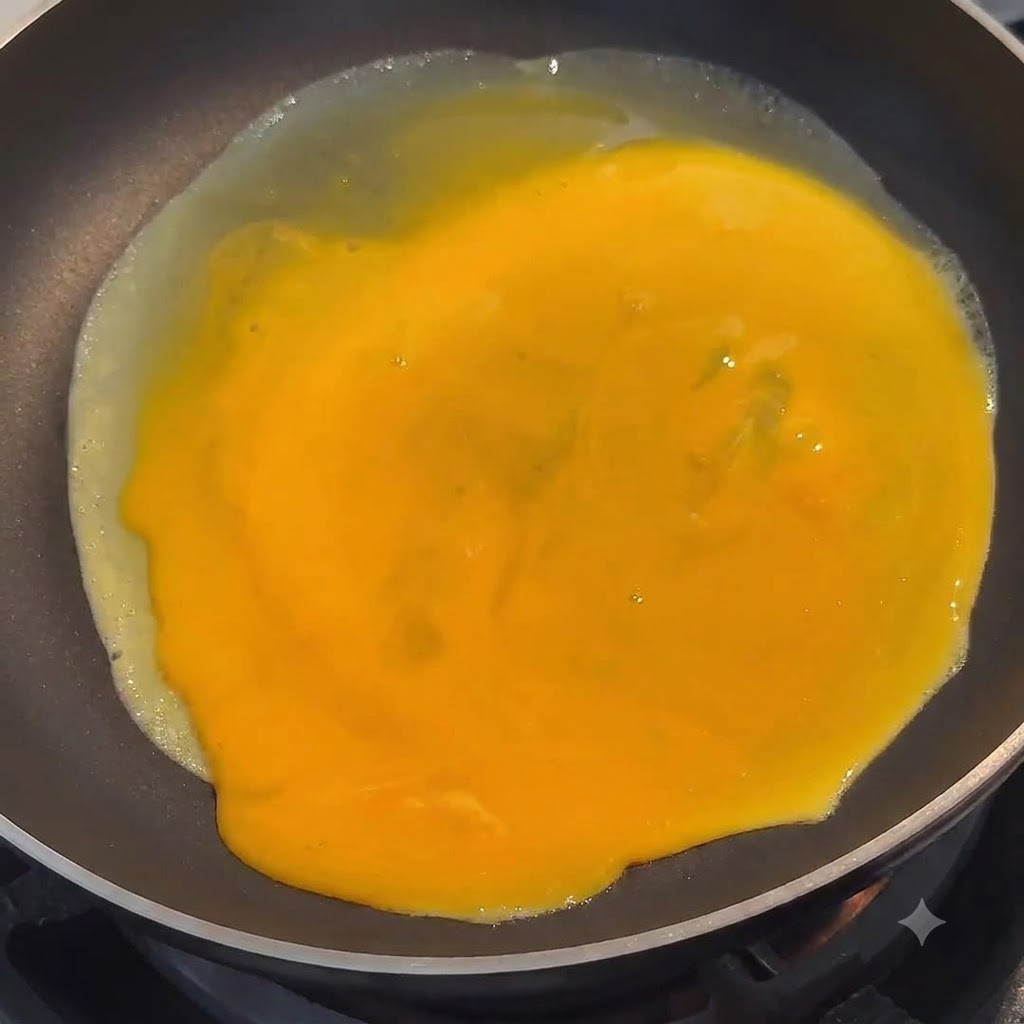 Huevo batido de color amarillo vibrante extendiéndose de manera uniforme por la superficie de una sartén negra.