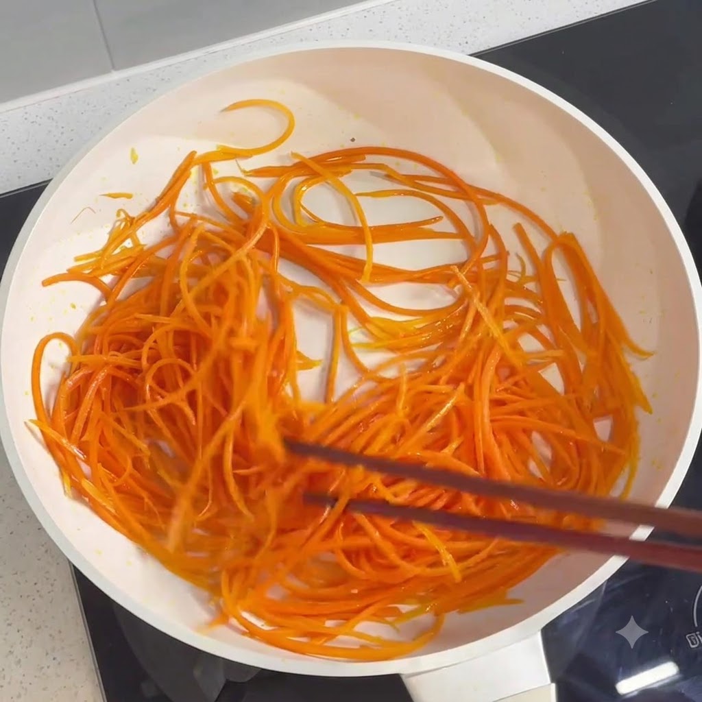 Zanahorias ralladas siendo salteadas y cocinadas en una sartén con palillos.