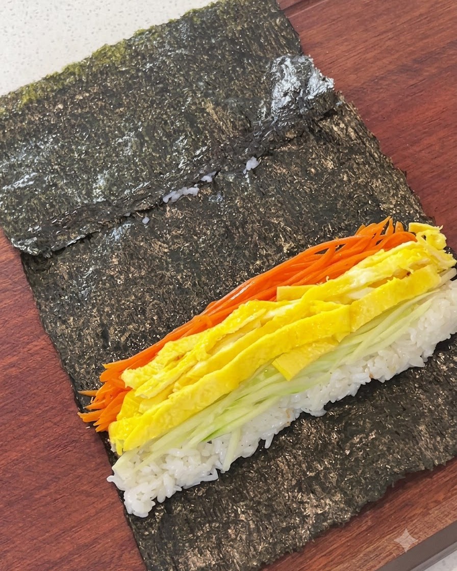 Zanahorias ralladas, tiras de huevo, pepino y pastel de pescado dispuestos sobre el arroz en una hoja de alga.