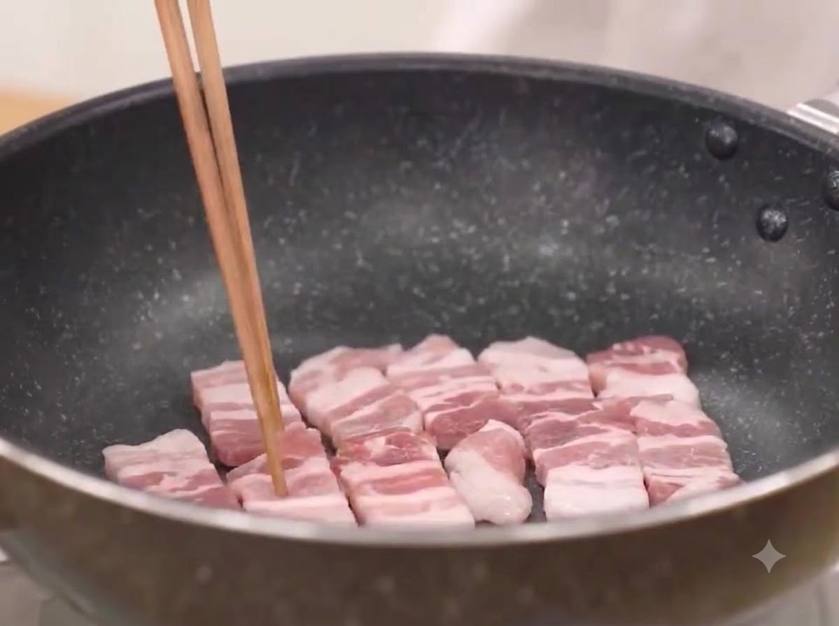 Rodajas de panceta de cerdo friéndose en una sartén caliente hasta que chisporroteen.