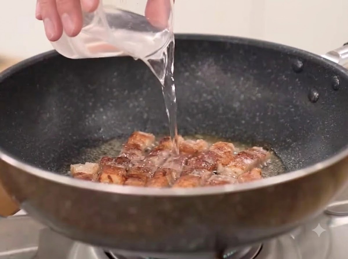 Agua, chile en polvo grueso y kimchi añadidos a la sartén con la panceta de cerdo frita.
