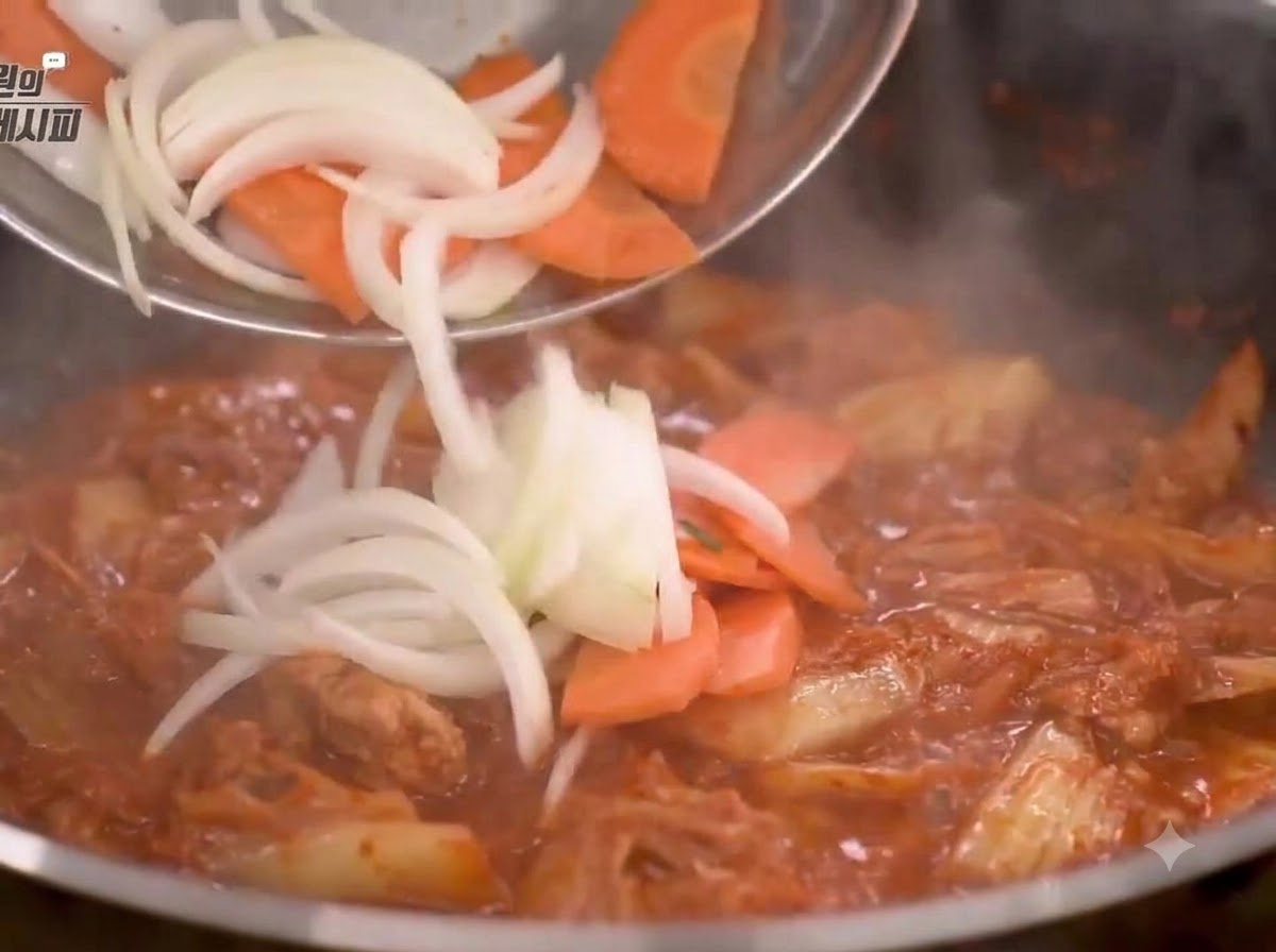 Cebollas y zanahorias cortadas añadidas a la sartén y salteadas con la mezcla de kimchi.