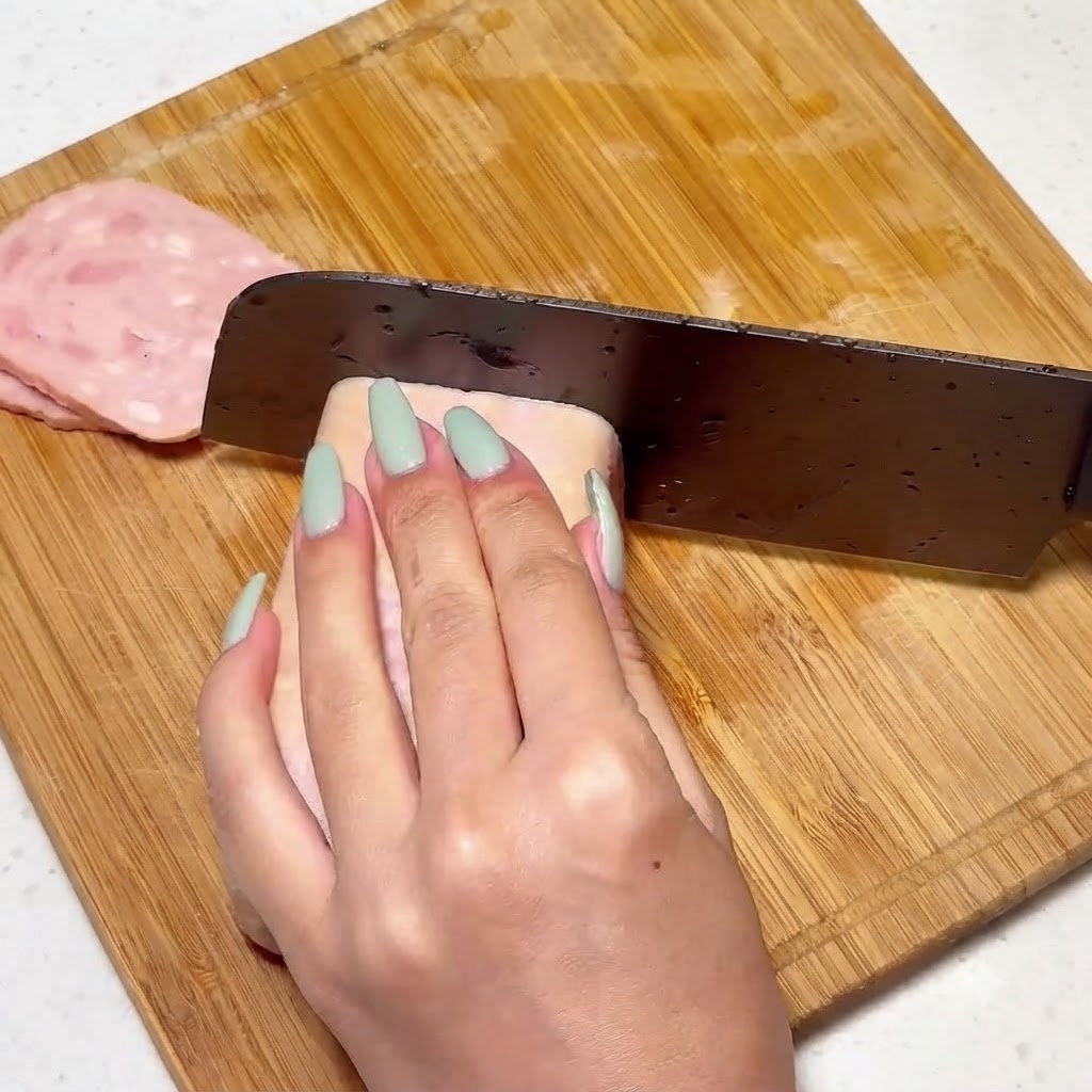 Carne enlatada siendo cortada uniformemente en una tabla de madera con un cuchillo.