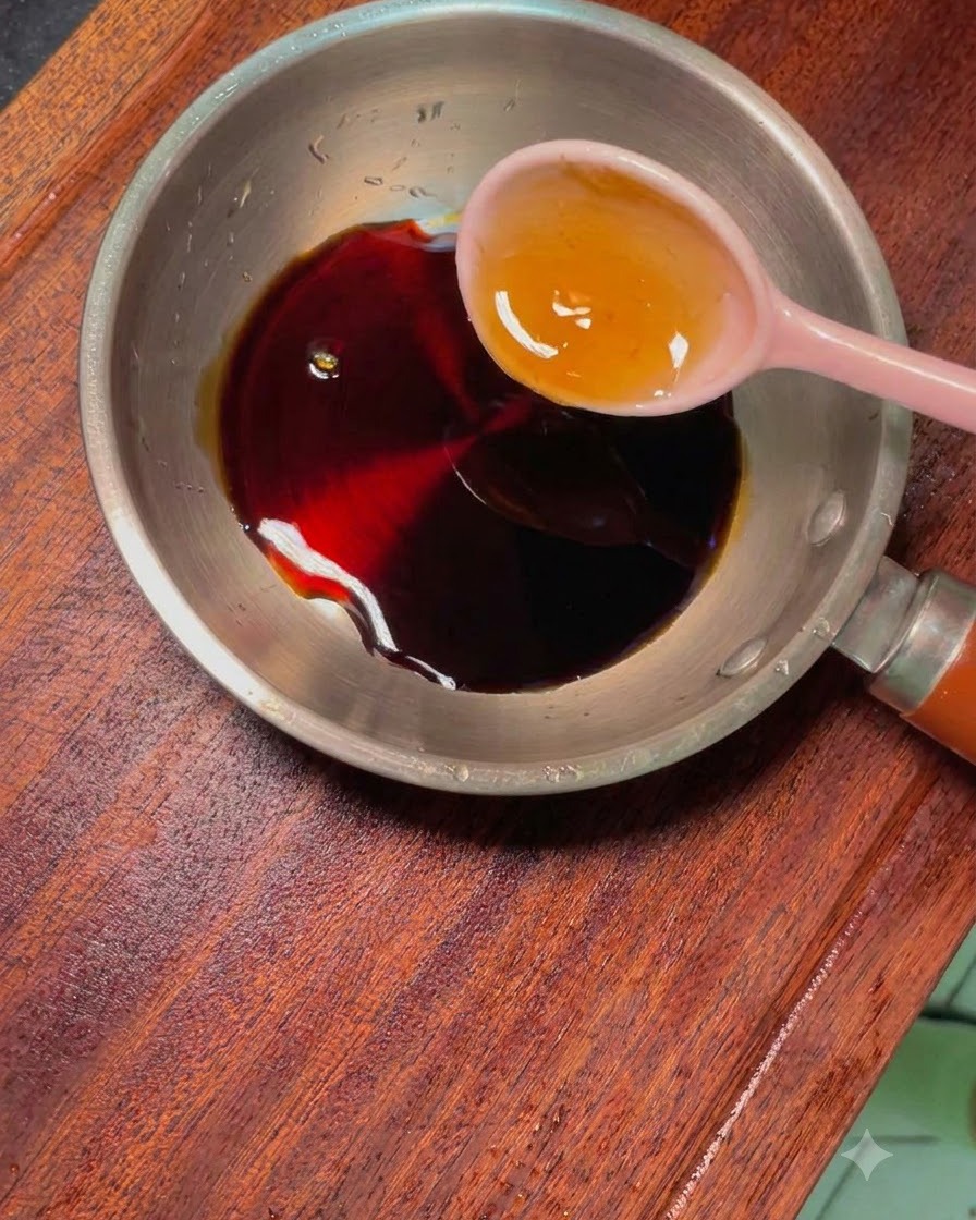 Una pequeña sartén metálica con salsa oscura y condimentos, con una cuchara rosa dentro.