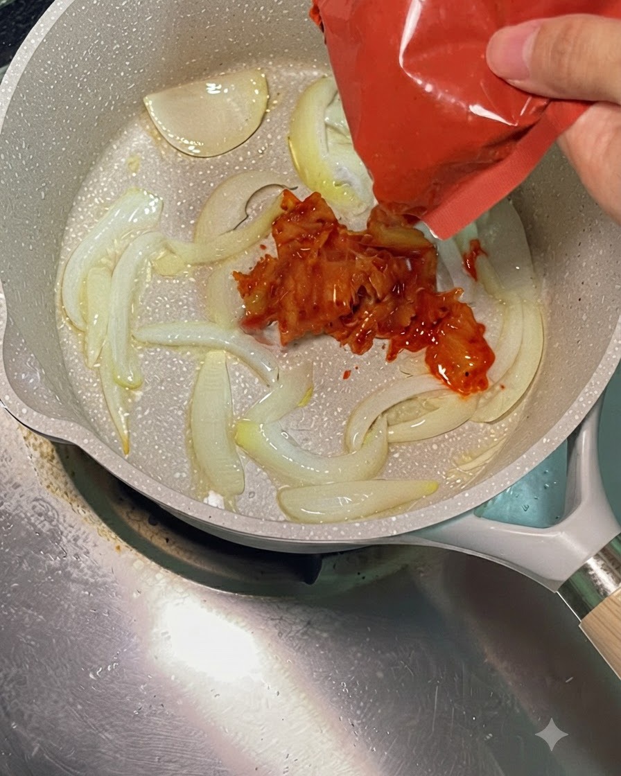 Kimchi picante troceado de color rojo añadiéndose desde su envase a la sartén con cebollas.