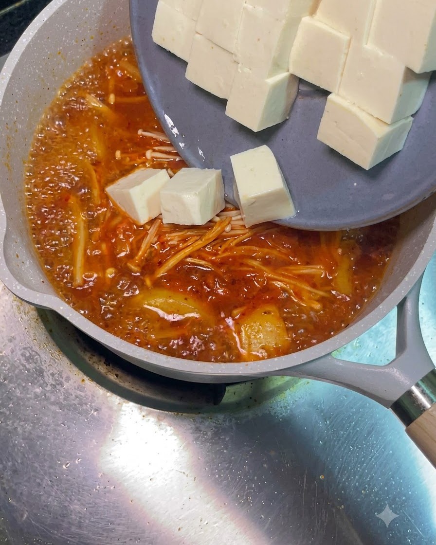 Cubos de tofu blanco deslizándose desde un plato gris hacia la sopa roja hirviendo.
