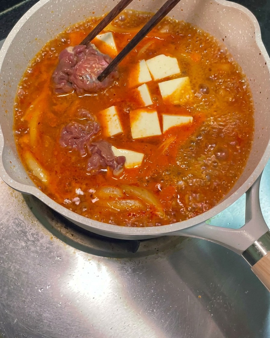 Palillos colocando láminas de ternera marinada cruda en la sartén con sopa roja hirviendo.