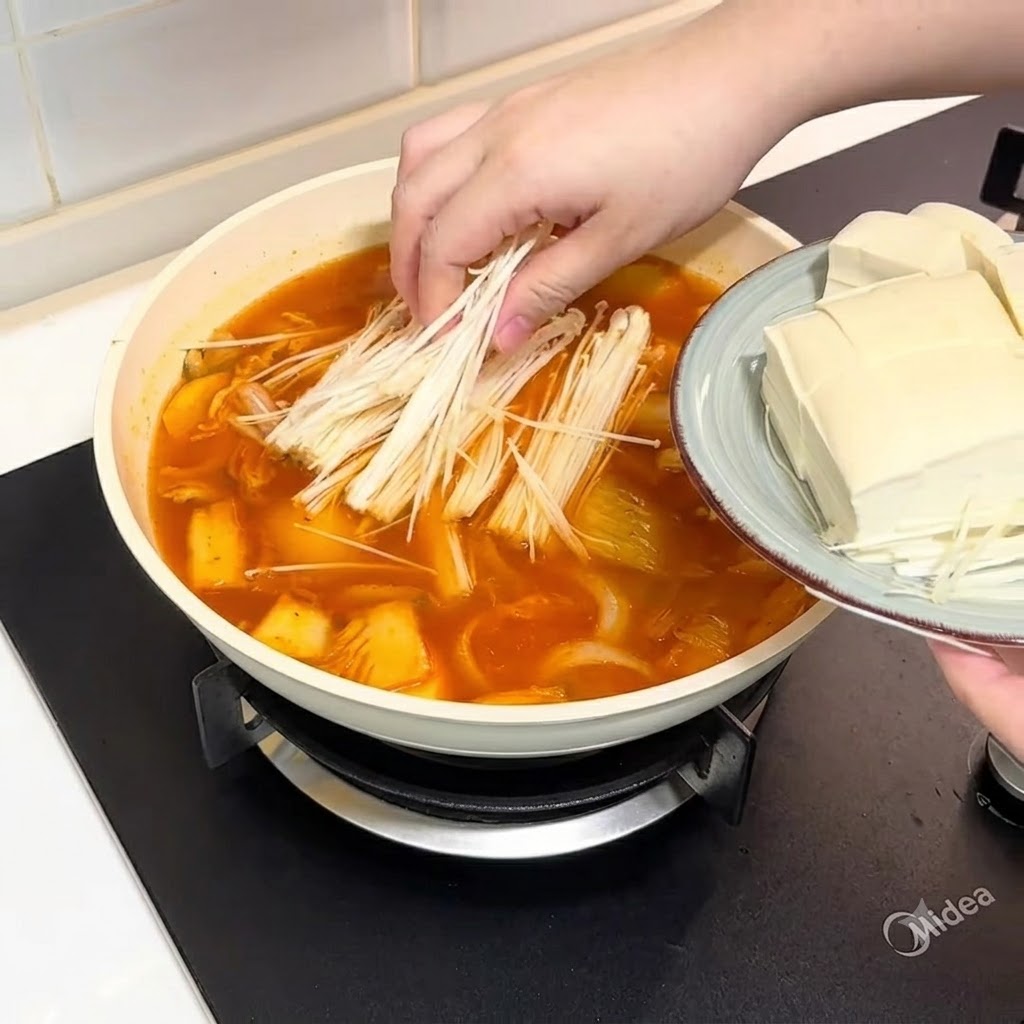 Champiñones enoki y tofú en rodajas colocándose dentro de la olla con el caldo.