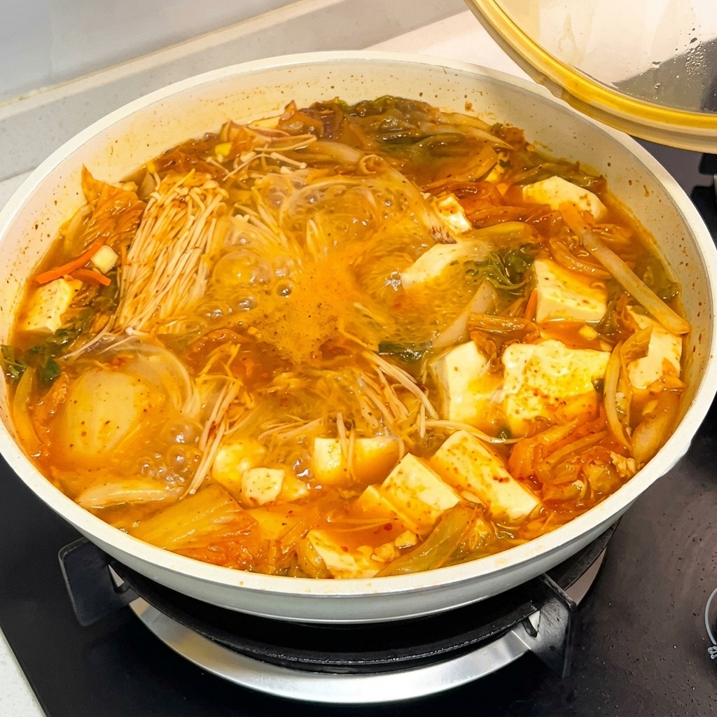 Una cucharada con salsa de pasta de chile coreano siendo vertida en una olla de sopa burbujeante.