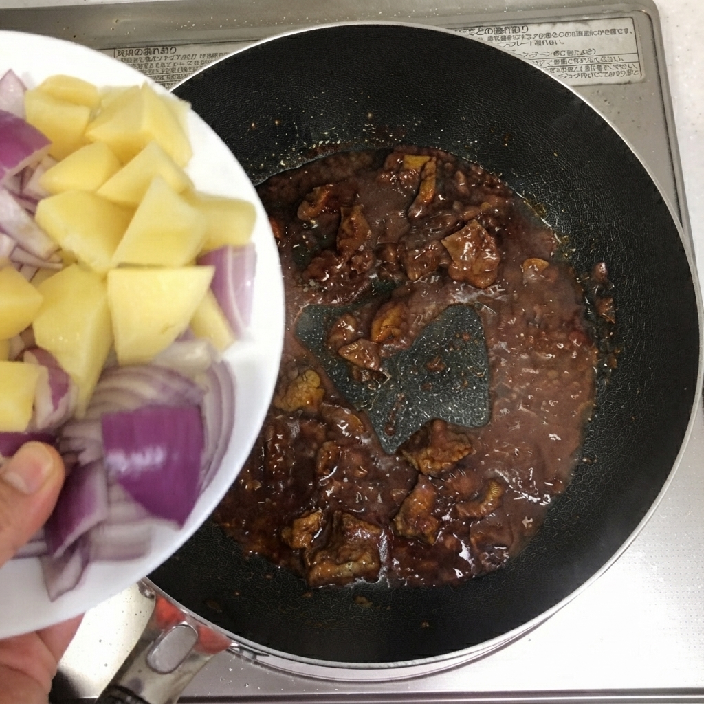 Patatas cortadas en rodajas y cebollas rojas siendo vertidas en la sartén con la ternera.