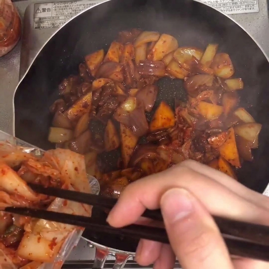 Kimchi siendo añadido a la sartén y mezclado con los demás ingredientes.