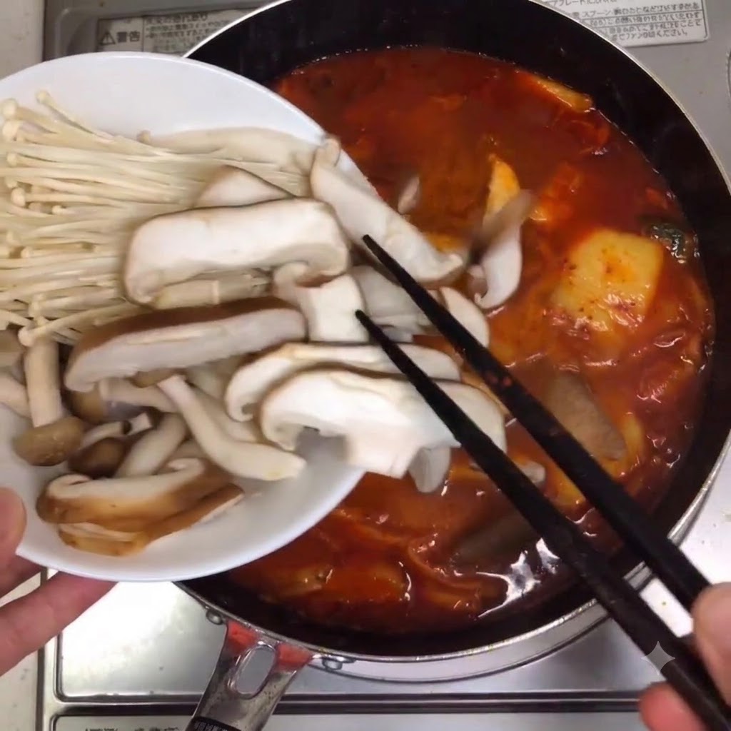 Setas surtidas y setas enoki siendo colocadas en la olla de sopa a fuego lento.