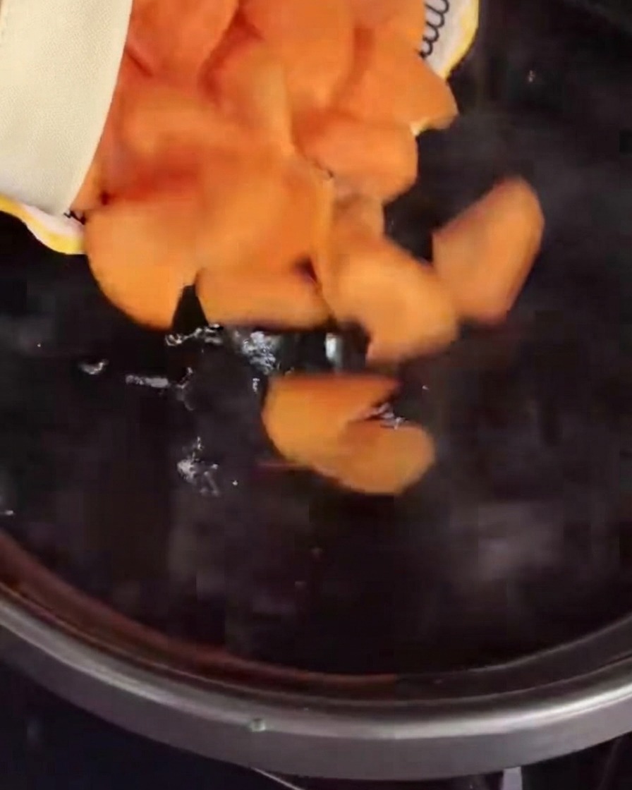 Zanahorias en rodajas siendo vertidas en una olla con agua hirviendo.
