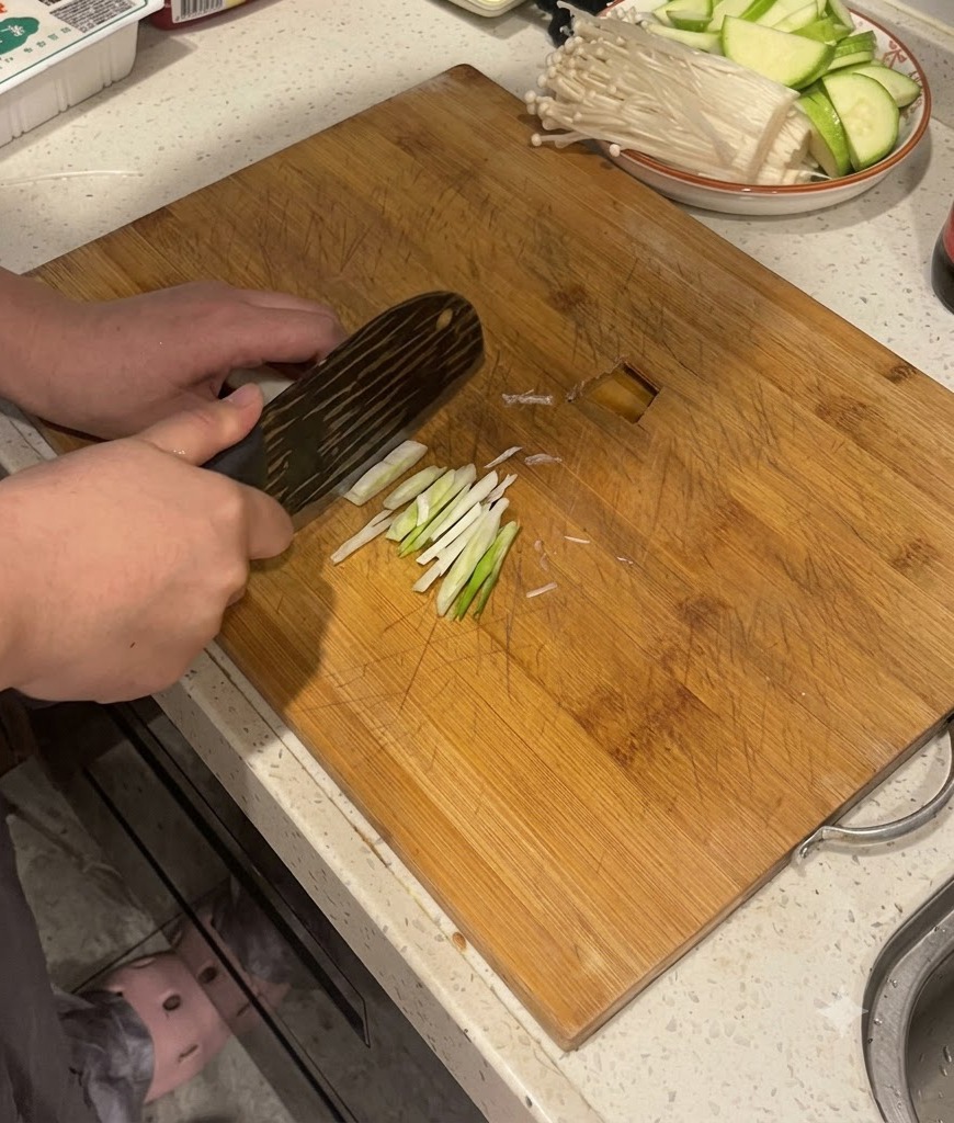 Manos usando un cuchillo de cocina para cortar tallos de cebollino en una tabla de cortar de madera.