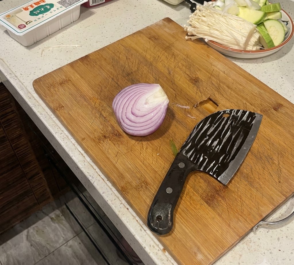 Una cebolla morada partida por la mitad sobre una tabla de cortar de madera junto a un cuchillo grande.
