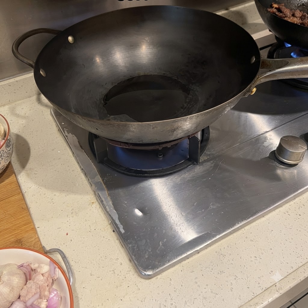 Panceta de cerdo y cebolla morada chisporroteando en un wok caliente con aceite.
