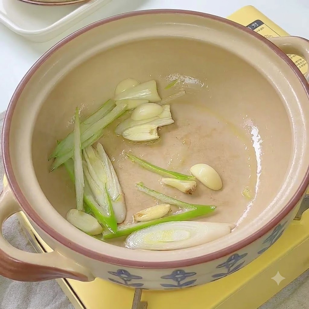Kimchi siendo sofrito con cebollines y ajo dentro de una olla de cerámica.