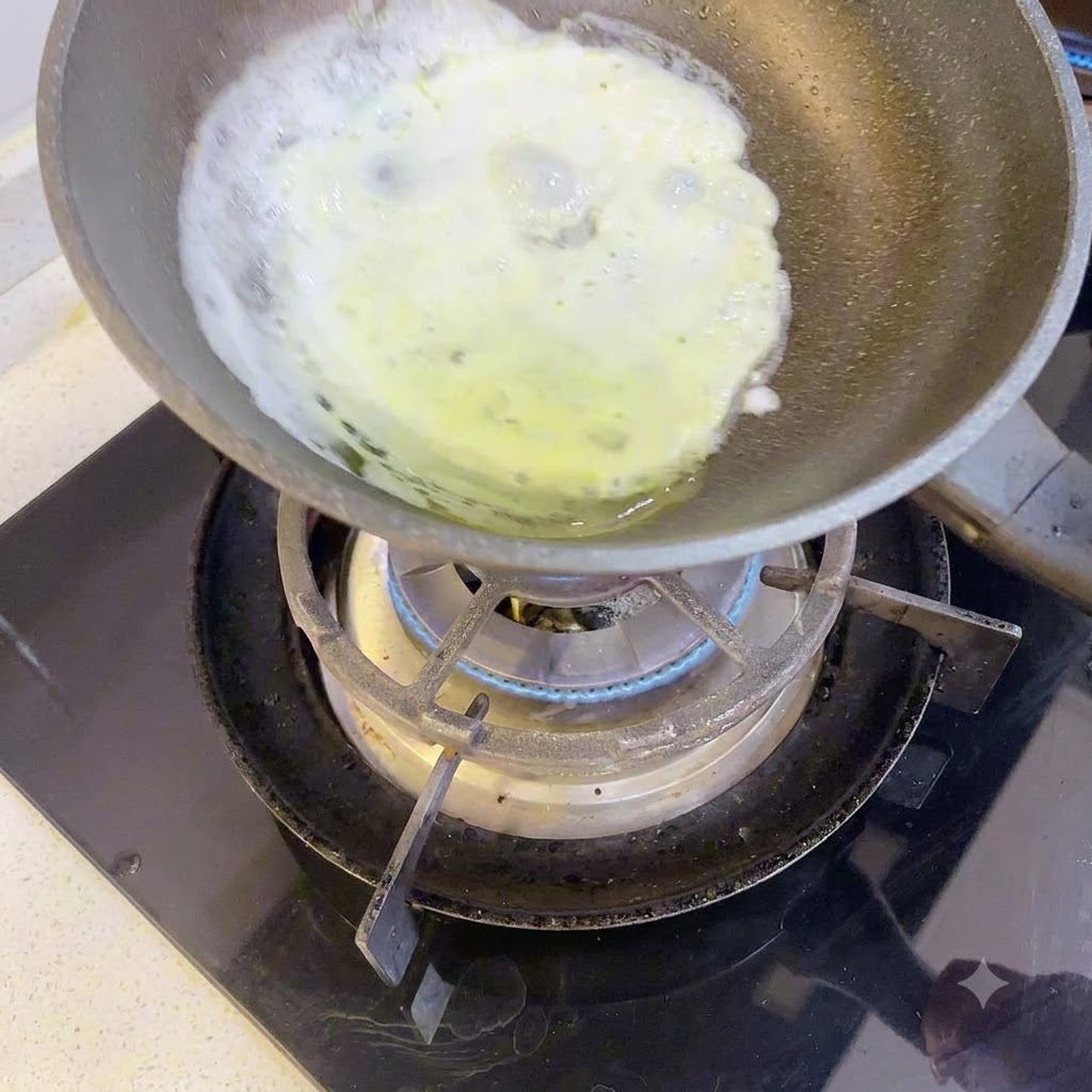 Una fina capa de clara de huevo cocinándose en una pequeña sartén sobre un quemador de gas.
