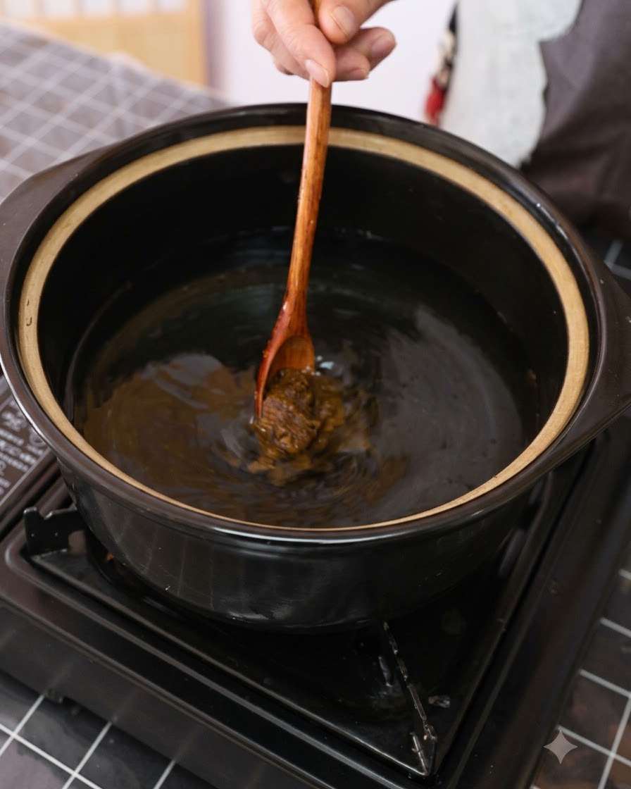 Pasta de soja marrón siendo revuelta en una olla con agua usando una cuchara de madera.