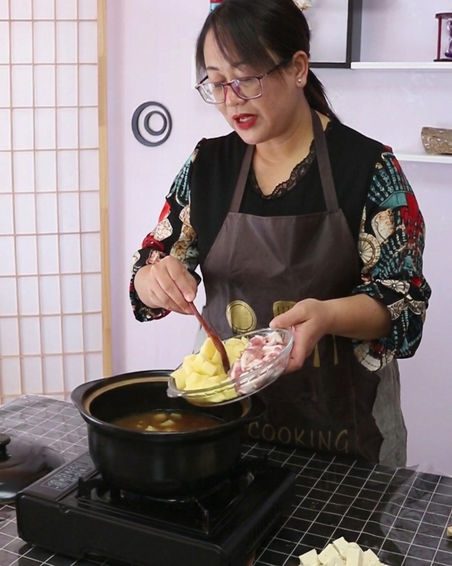 Patatas en dados y panceta de cerdo cortada siendo vertidas desde un plato de vidrio en la olla de cocina.