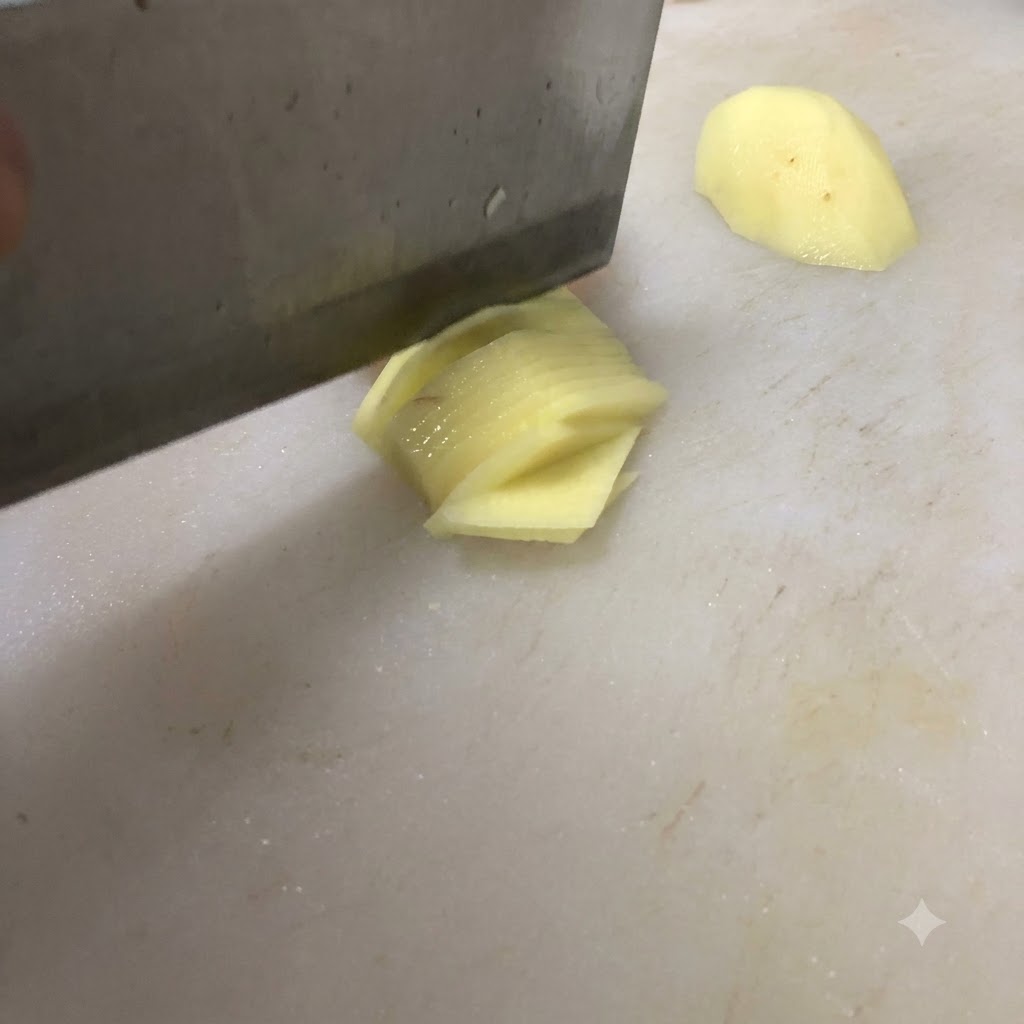 Un cuchillo cortando una patata en trozos finos sobre una tabla de cortar blanca.