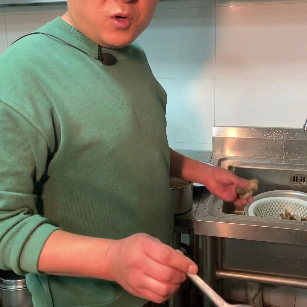Almejas frescas siendo añadidas a una olla de estofado de pasta de soja hirviendo a fuego lento.