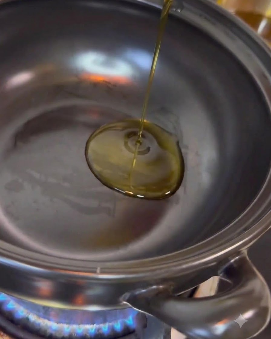 Aceite de cocina transparente siendo vertido en el centro de una olla de acero inoxidable colocada sobre una llama azul activa.