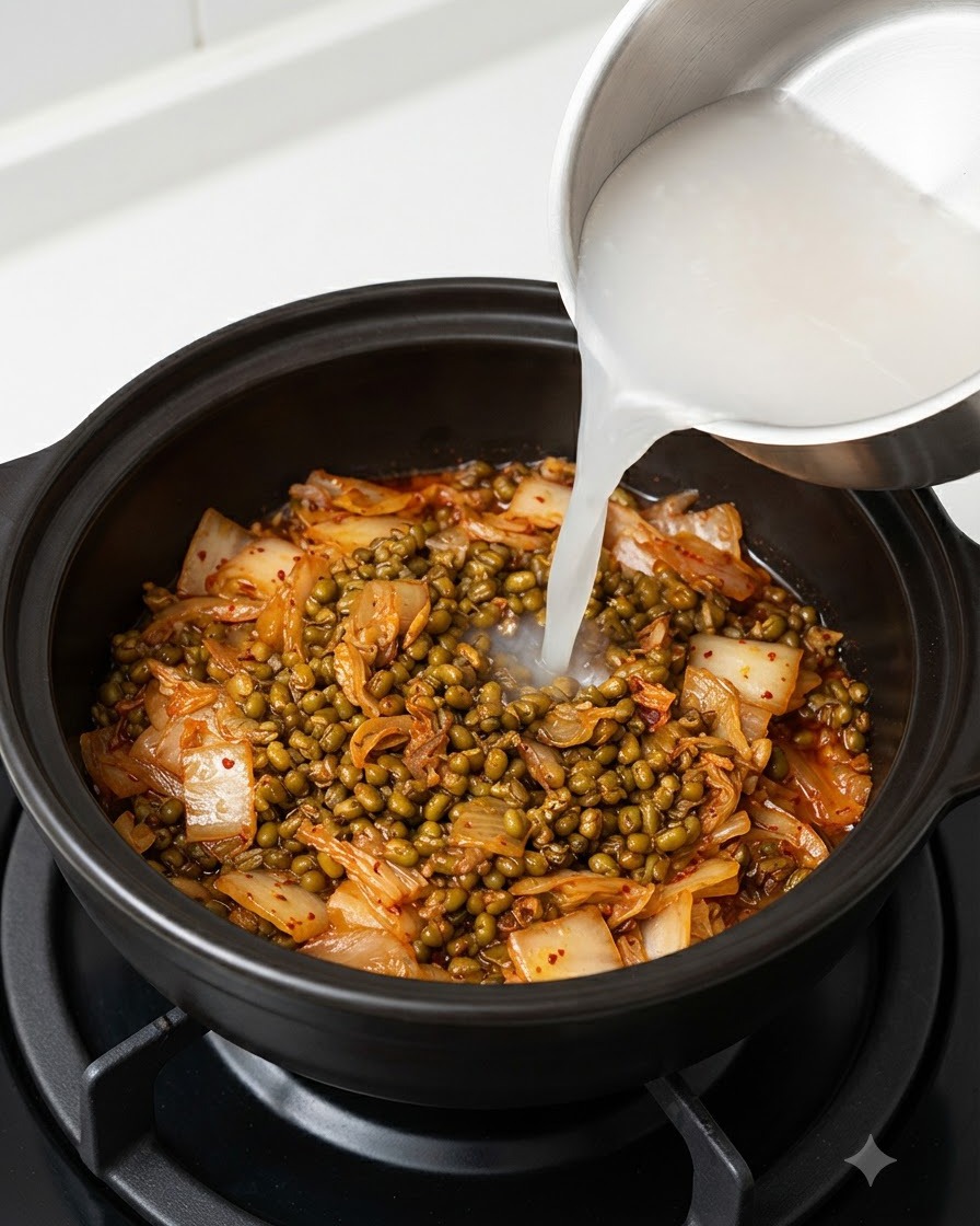 Agua de lavado de arroz blanca y turbia siendo vertida desde una olla de acero en una olla oscura que contiene kimchi y soja fermentada.