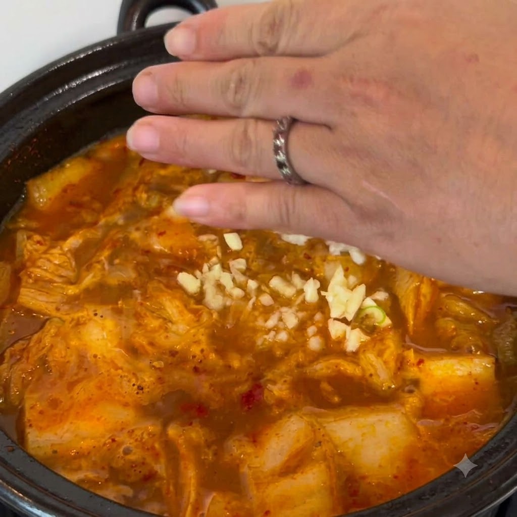 Ajo picado siendo esparcido a mano en la olla de estofado burbujeante.