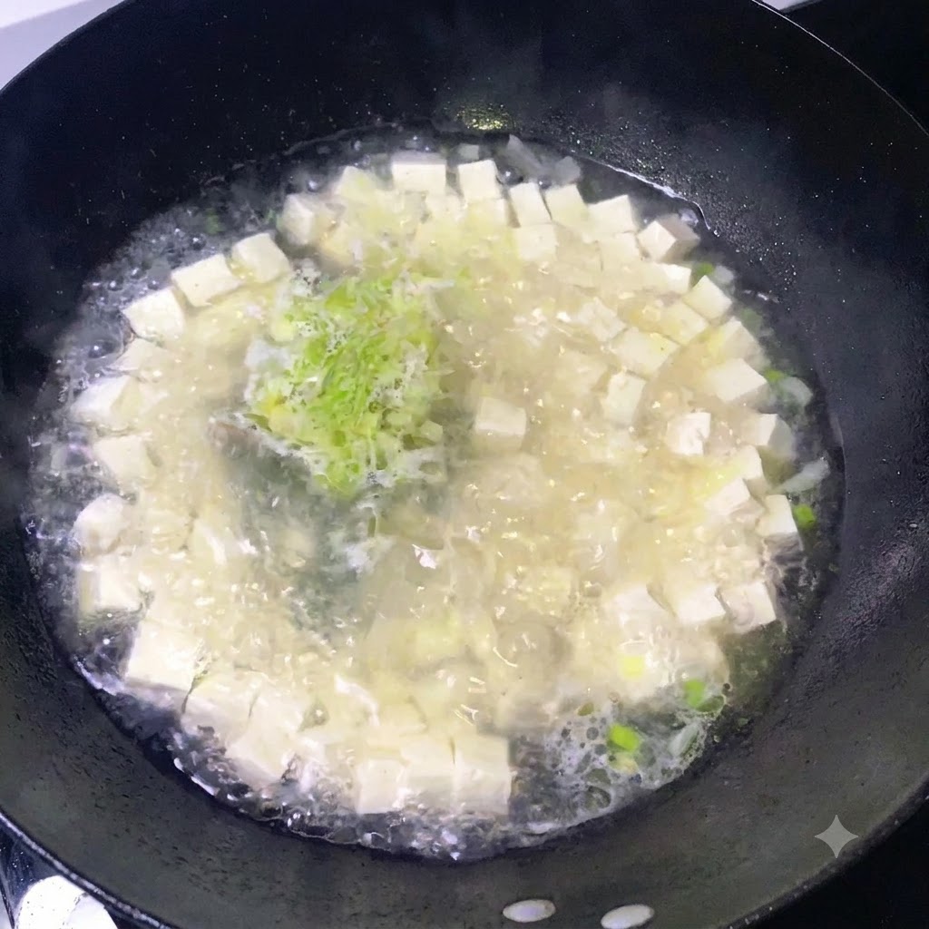 Condimentos siendo esparcidos sobre una olla hirviendo de sopa de tofu y cebollino picado.