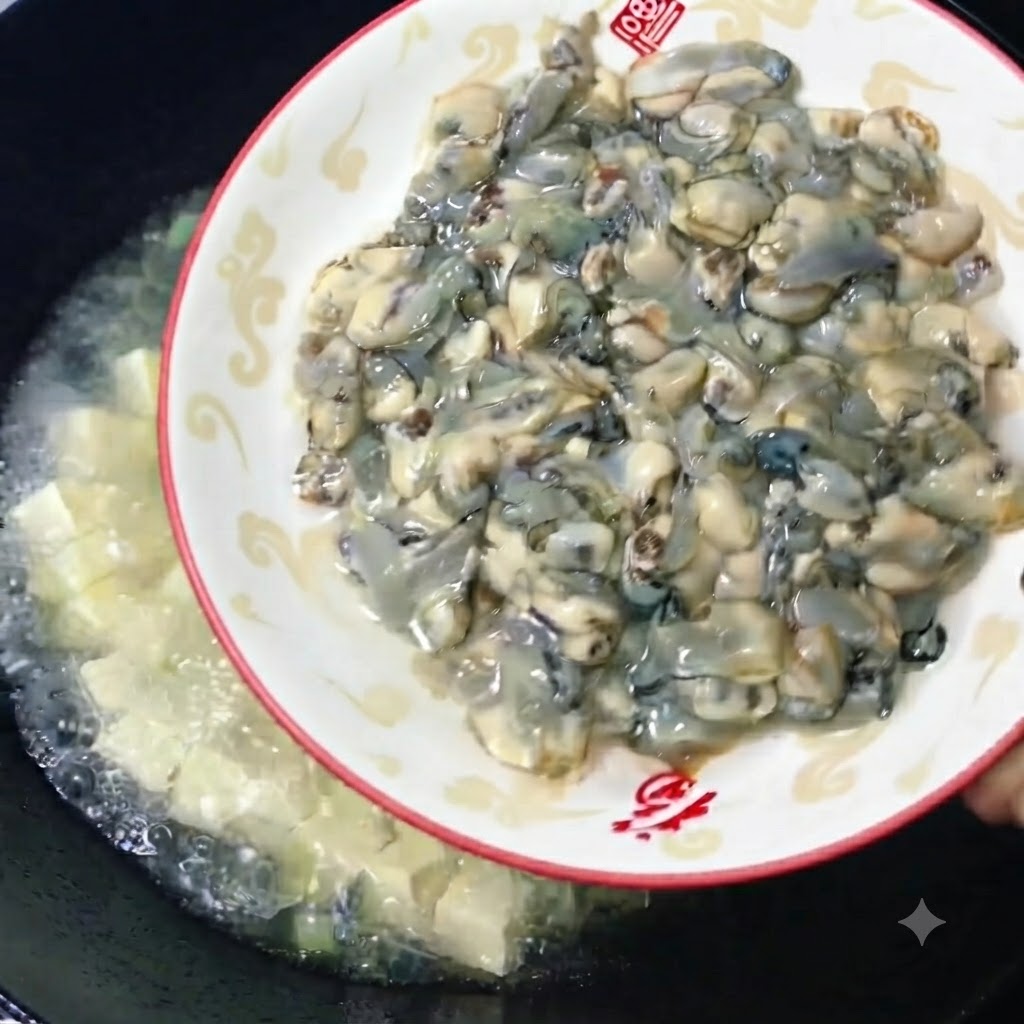 Ostras crudas frescas y regordetas siendo deslizadas desde un plato decorativo hacia un wok con caldo de tofu a fuego lento.