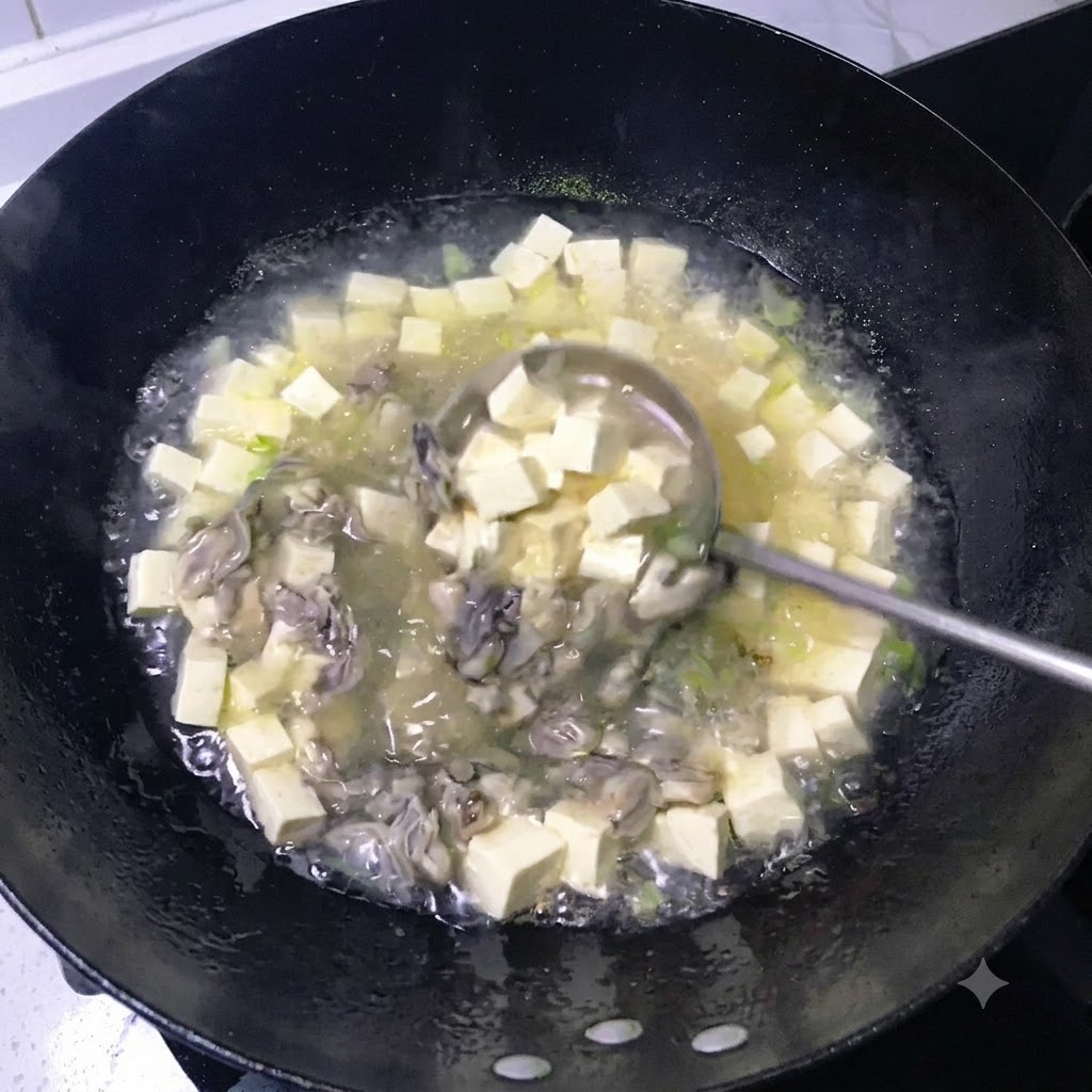 Un cucharón revolviendo un caldo blanco lechoso a fuego lento lleno de tofu en dados y ostras cocidas en un wok negro.