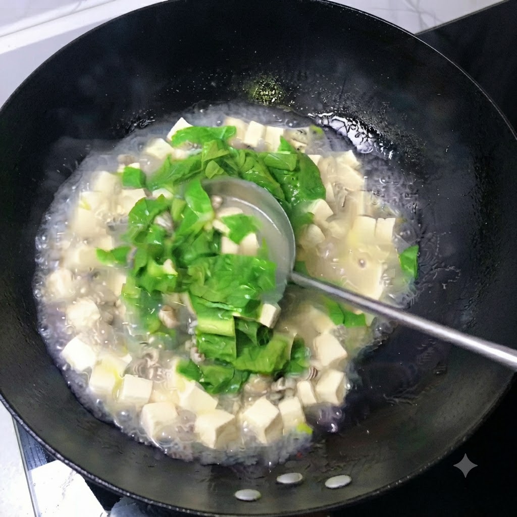 Un cucharón removiendo un caldo blanco lechoso lleno de cubos de tofu, ostras y hojas verdes en un wok.