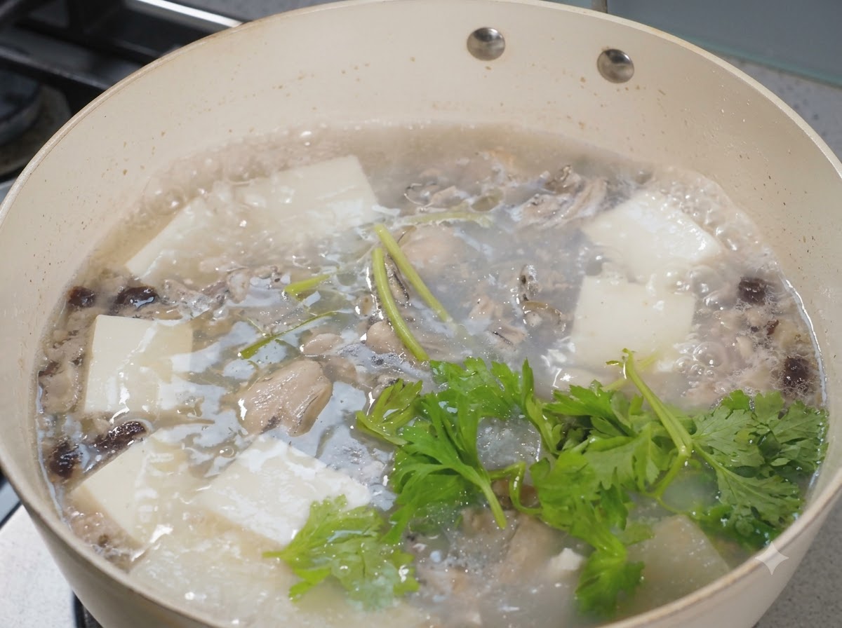 Hojas de apio fresco esparcidas sobre una olla burbujeante de sopa de ostras y tofu.