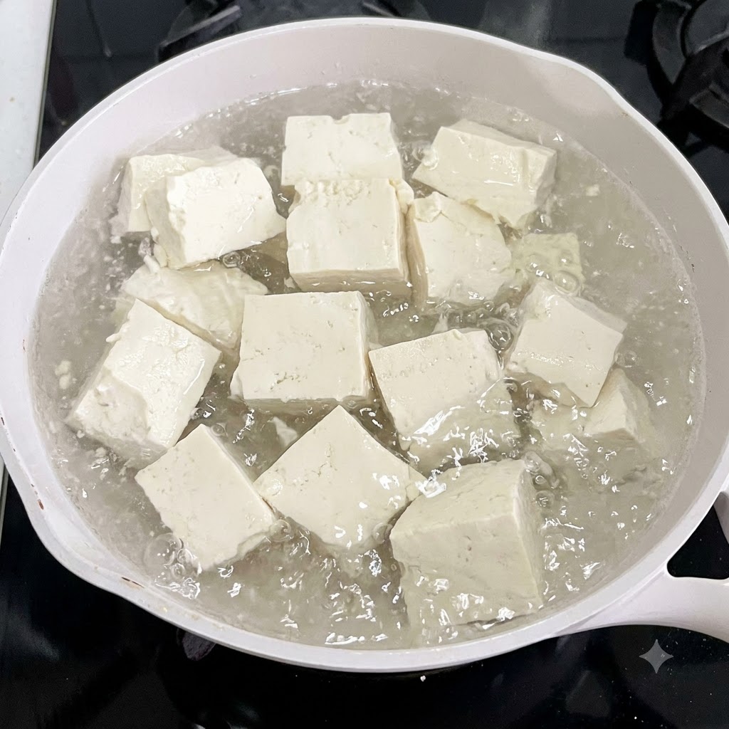Cubos de tofu hirviendo en una olla blanca de agua con rodajas de jengibre.