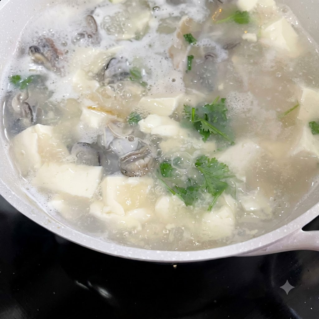 Cilantro y cebollino picados siendo añadidos a una olla hirviendo de sopa de ostras y tofu.