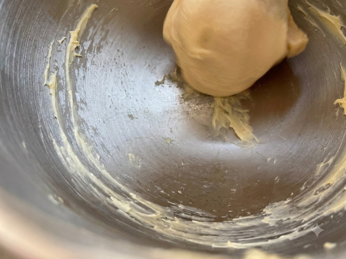 Una bola lisa de masa de levadura reposando dentro de un bol de metal con restos de mantequilla en los bordes.