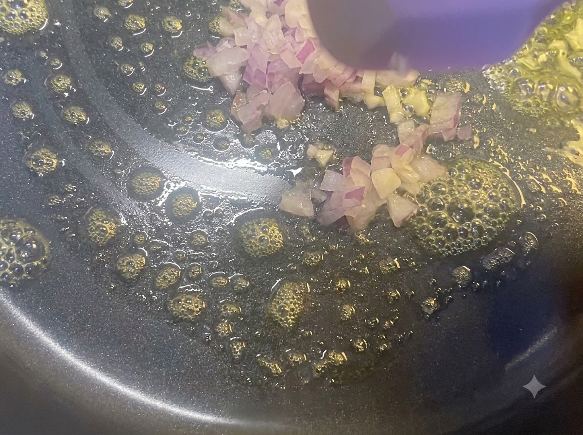 Cebollas rojas picadas salteándose en una sartén con mantequilla derretida usando una espátula de madera.