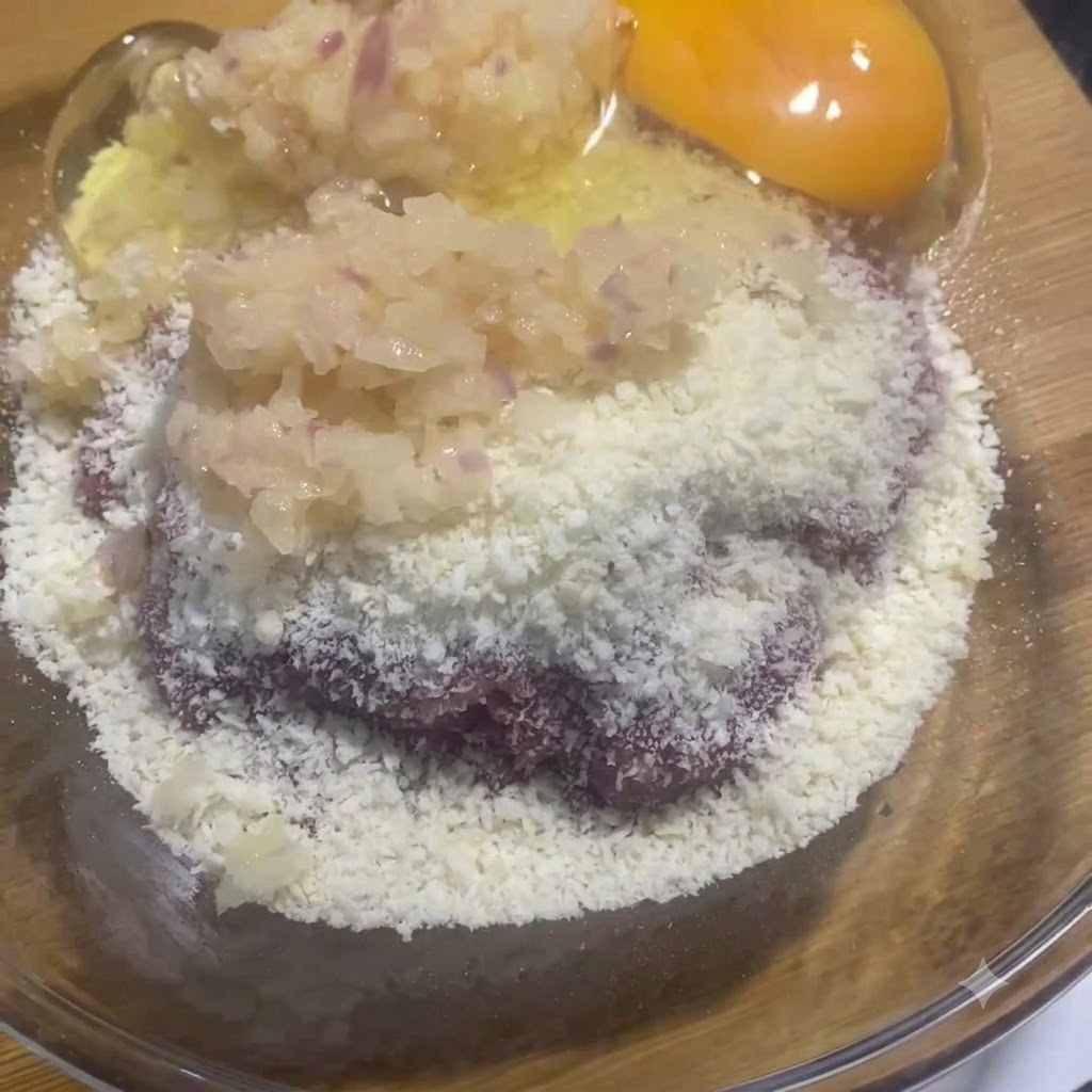 Una yema y clara de huevo crudo en el bol de vidrio junto con la mezcla de carne y cebolla.