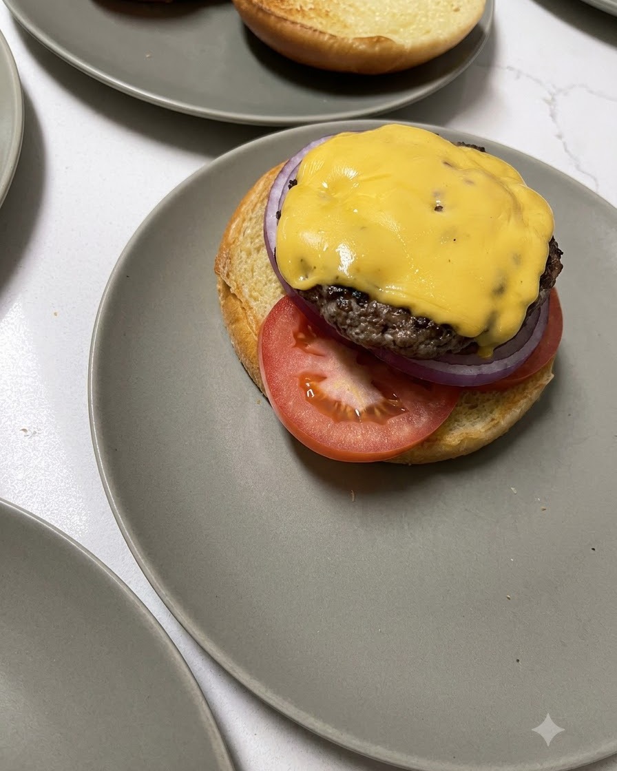Una hamburguesa de ternera cubierta de queso siendo transferida con una espátula de madera sobre la base de un pan.