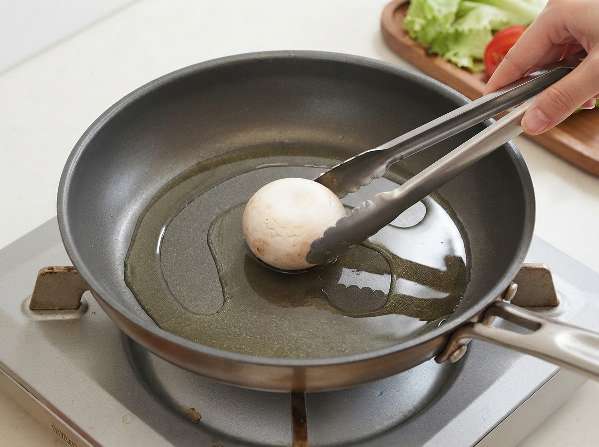 Un solo champiñón siendo colocado en una sartén aceitada con pinzas.