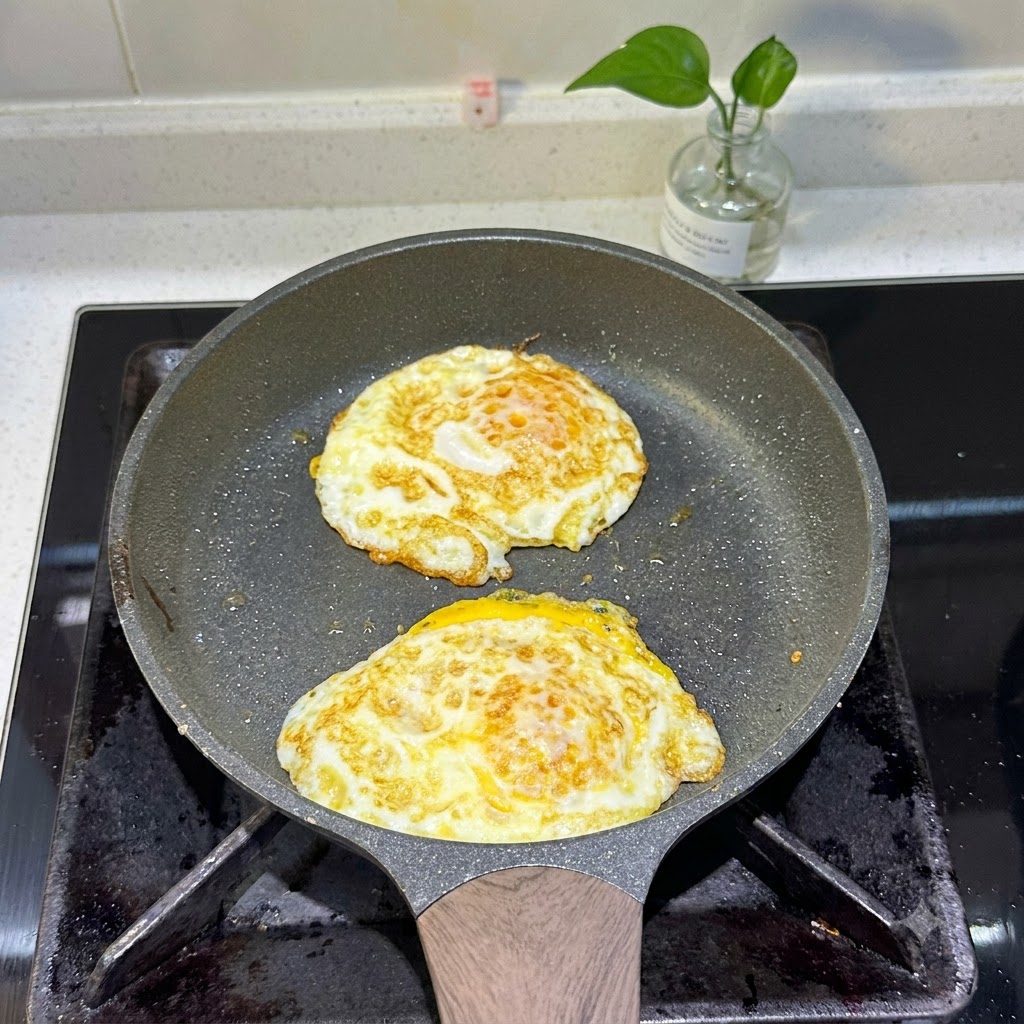 Dos huevos fritos cocinándose en una sartén con bordes dorados.