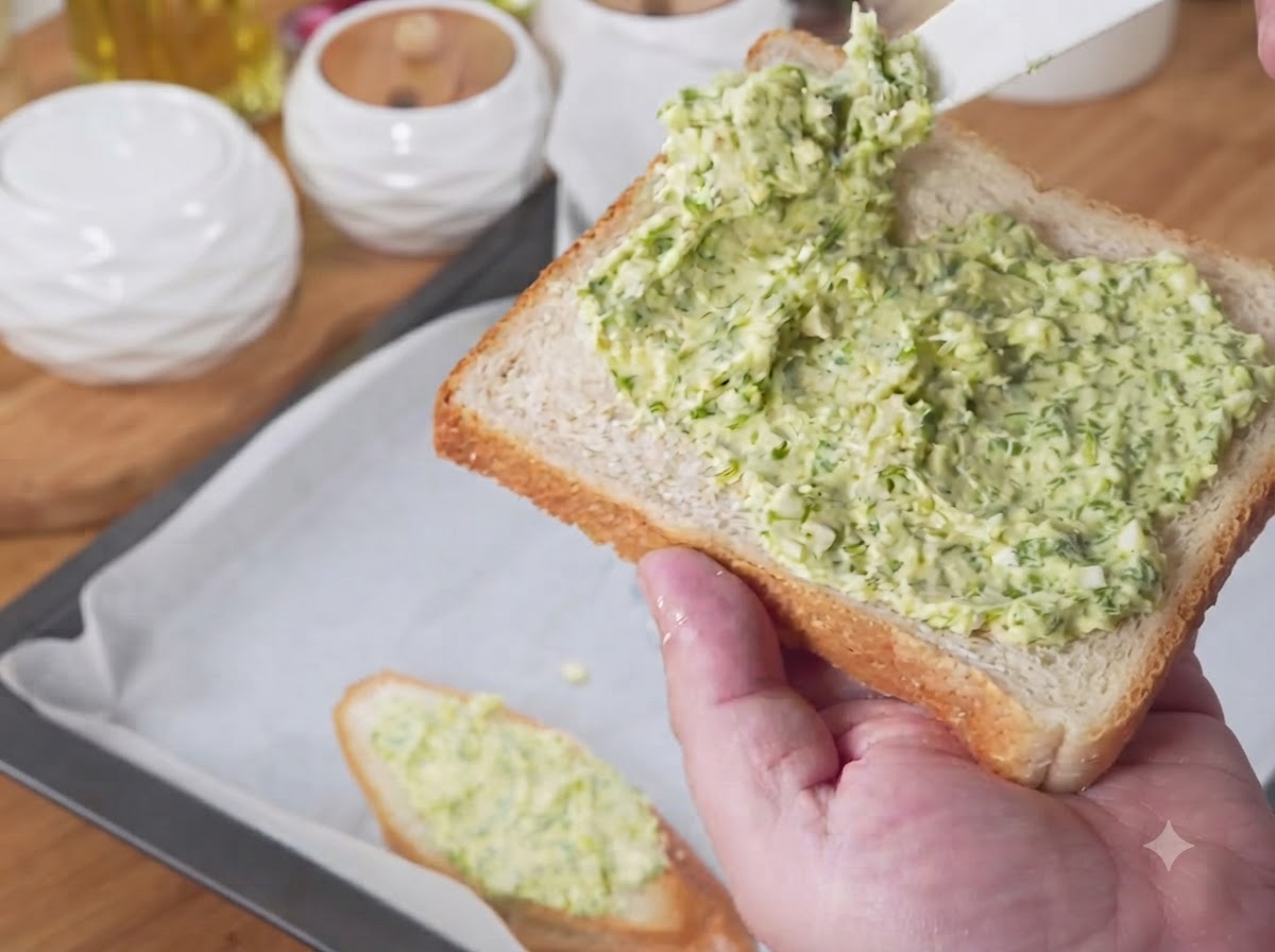 Rebanadas de pan cubiertas con la mezcla de mantequilla de ajo verde dispuestas en una bandeja para hornear forrada con papel pergamino.