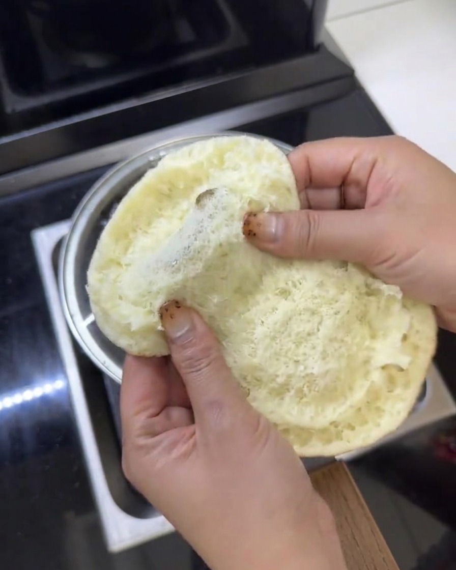 Hojas de lechuga verde fresca siendo colocadas dentro de un pan de hamburguesa de mantequilla abierto.