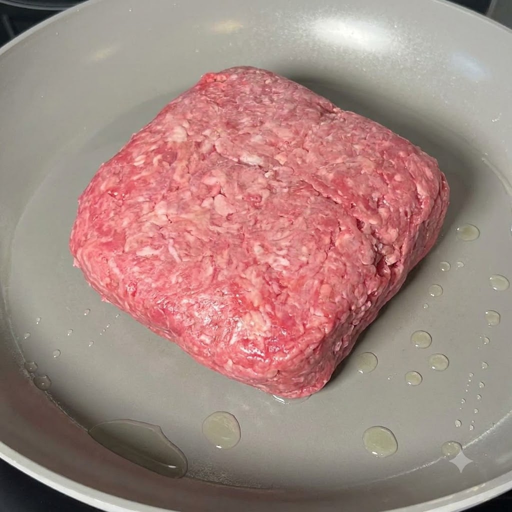 Carne picada cocinándose y desmoronándose con una espátula de madera en una sartén ancha.