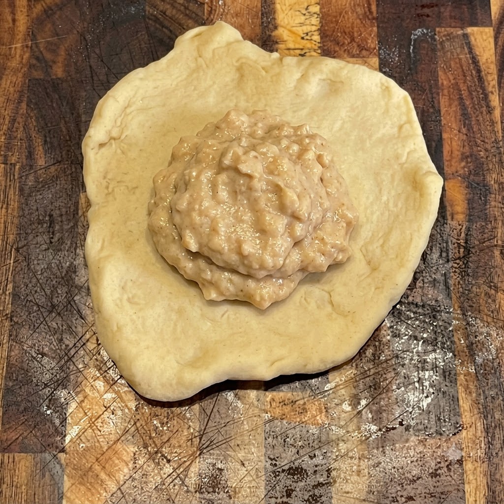 Salsa de hamburguesa extendida ordenadamente sobre una pieza redonda y plana de masa en una tabla de madera.