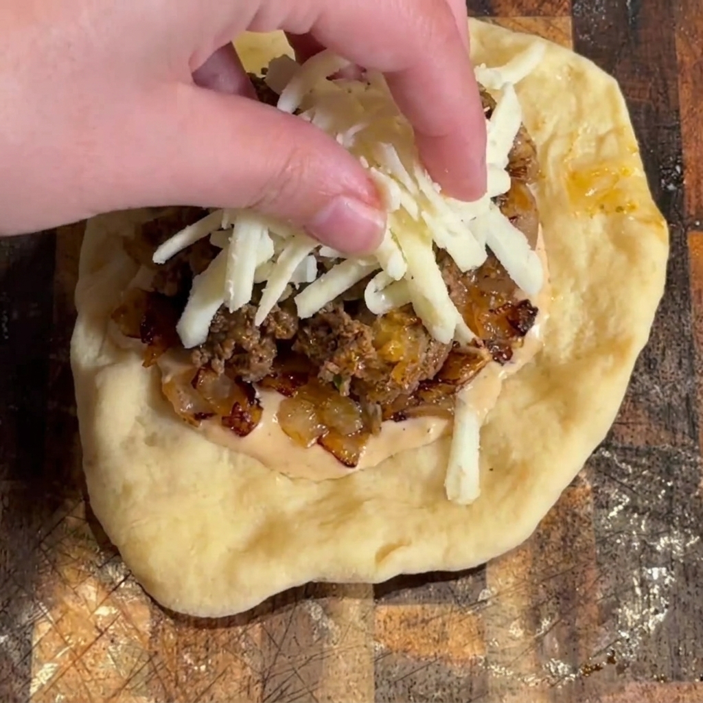 Queso mozzarella rallado siendo espolvoreado encima del relleno de la hamburguesa.