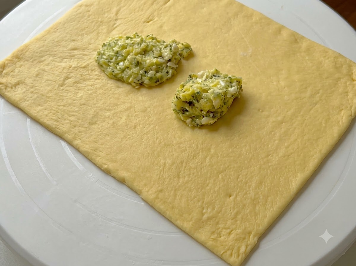 Porciones de crema de mantequilla de ajo verde situadas sobre una lámina rectangular de masa aplanada.