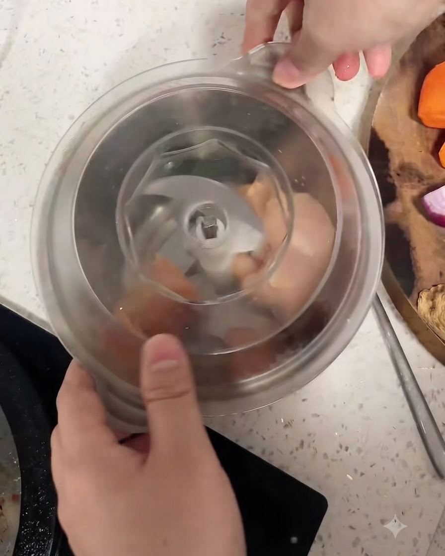 Trozos crudos de pechuga de pollo dentro del vaso de un procesador de alimentos alrededor de la cuchilla central.